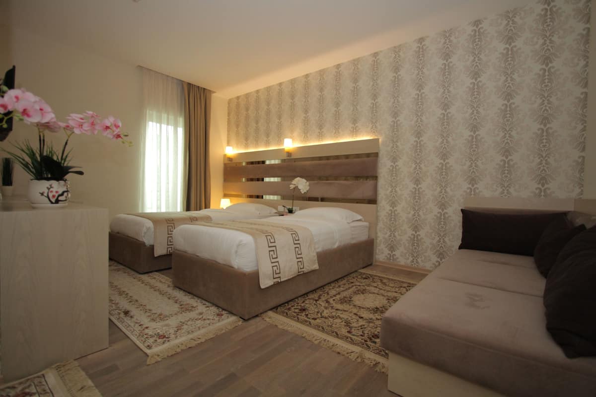 A hotel room with two beds, a sofa, a decorative vase with flowers, and a patterned wallpaper.