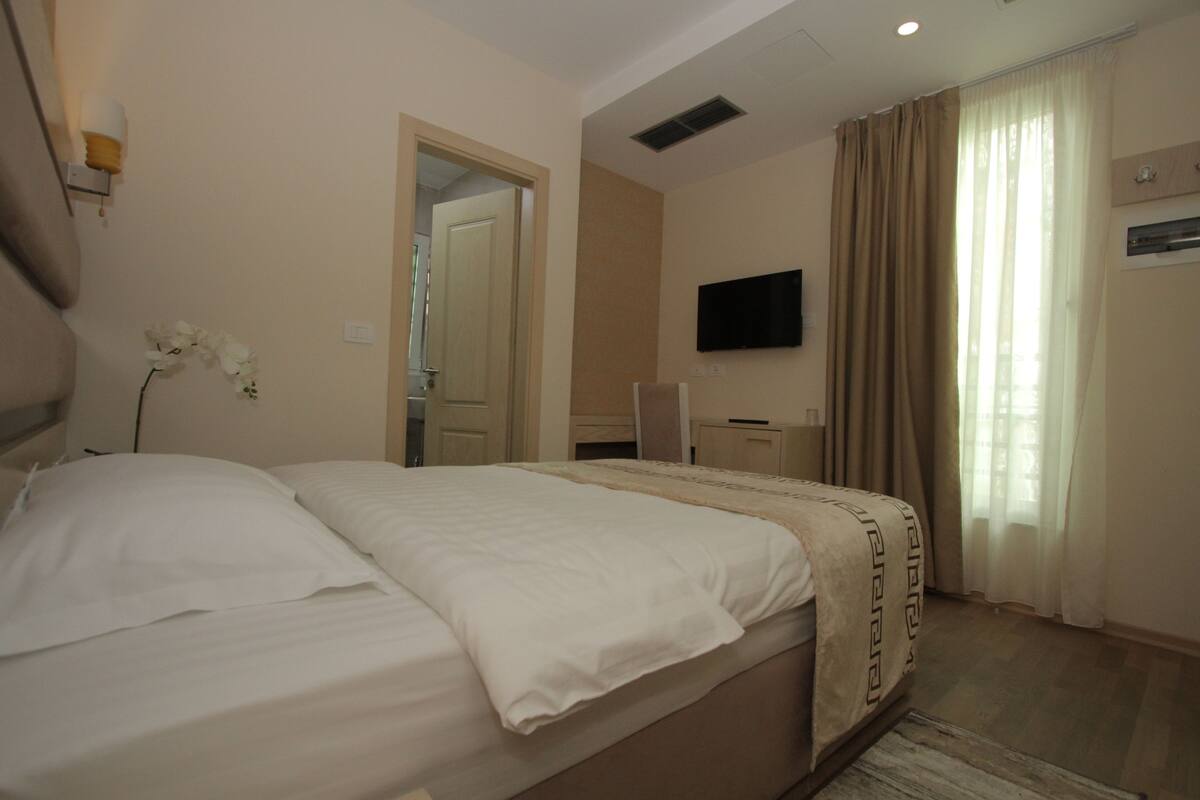 A hotel room with a bed, a television mounted on the wall, and a window with curtains.