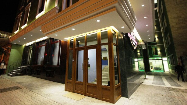 A hotel entrance with a glass facade, a staircase leading to the entrance, and a person walking away. - Capital Tirana Hotel (Tirana)