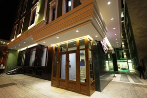 Fachada de vidrio de un hotel, una escalera que conduce a la entrada, y una persona alejándose.