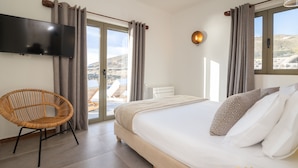 Ein Schlafzimmer mit Bett, Sessel, Fernseher und Blick ins Freie.