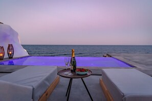 A poolside setting with lounge chairs, a table with a bottle and glasses, and a bowl of fruit. - Casa Di Mare (Santorini)