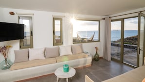 Ein modernes Wohnzimmer mit einer Couch, einem Flachbildfernseher und großen Fenstern mit Blick aufs Meer.