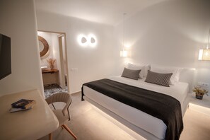 A modern bedroom with a large bed, bedside lamps, and a small table with books. - Casa Di Mare (Santorini)