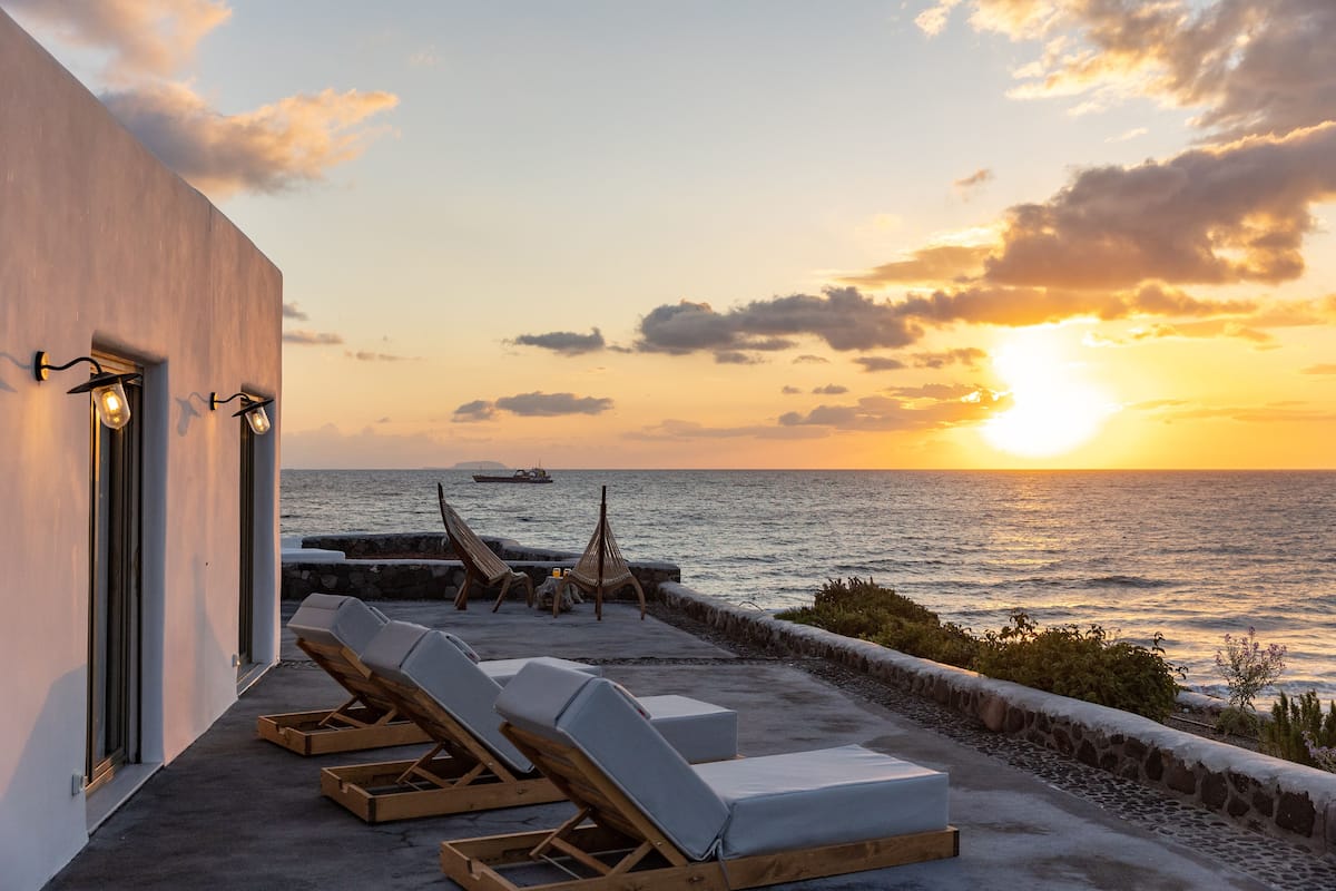 A sunset view from a balcony with lounge chairs and a stone wall.