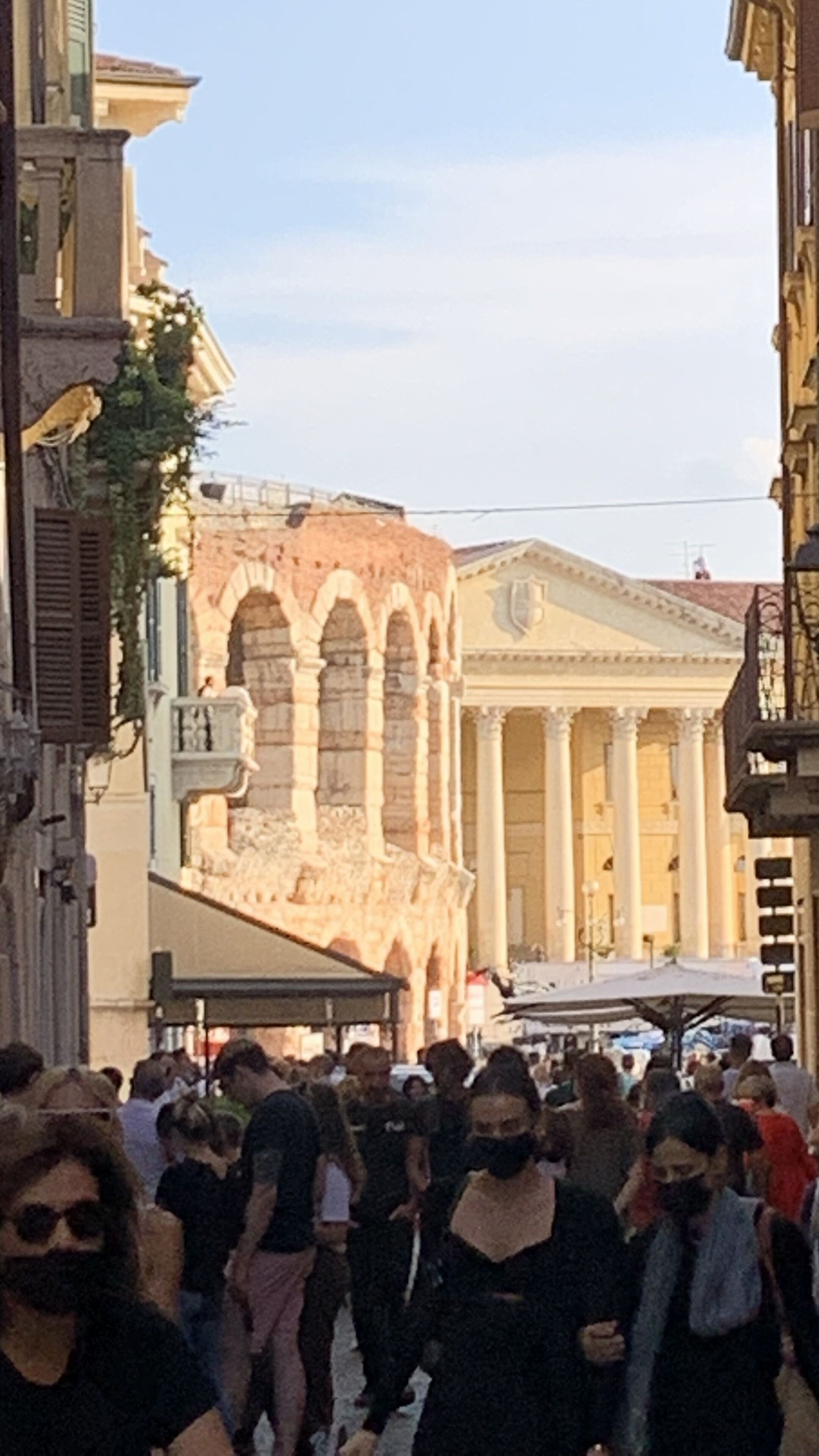 Eine belebte Straße mit historischen Gebäuden, darunter ein Bauwerk mit Säulen und ein Gebäude mit Rundbogenfenstern.