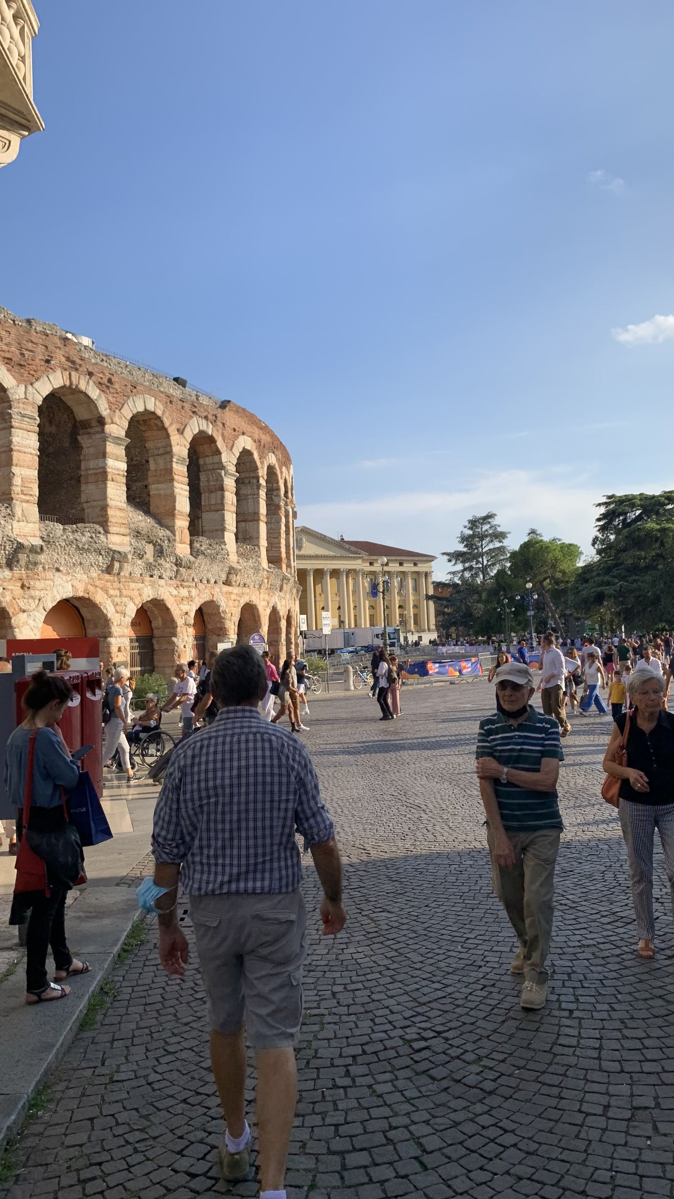 A cobblestone street with tourists walking towards an ancient amphitheater.