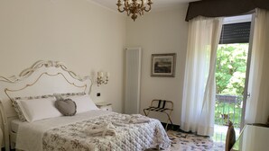 Un dormitorio con cama, un radiador, una silla, una ventana con cortinas y una araña.