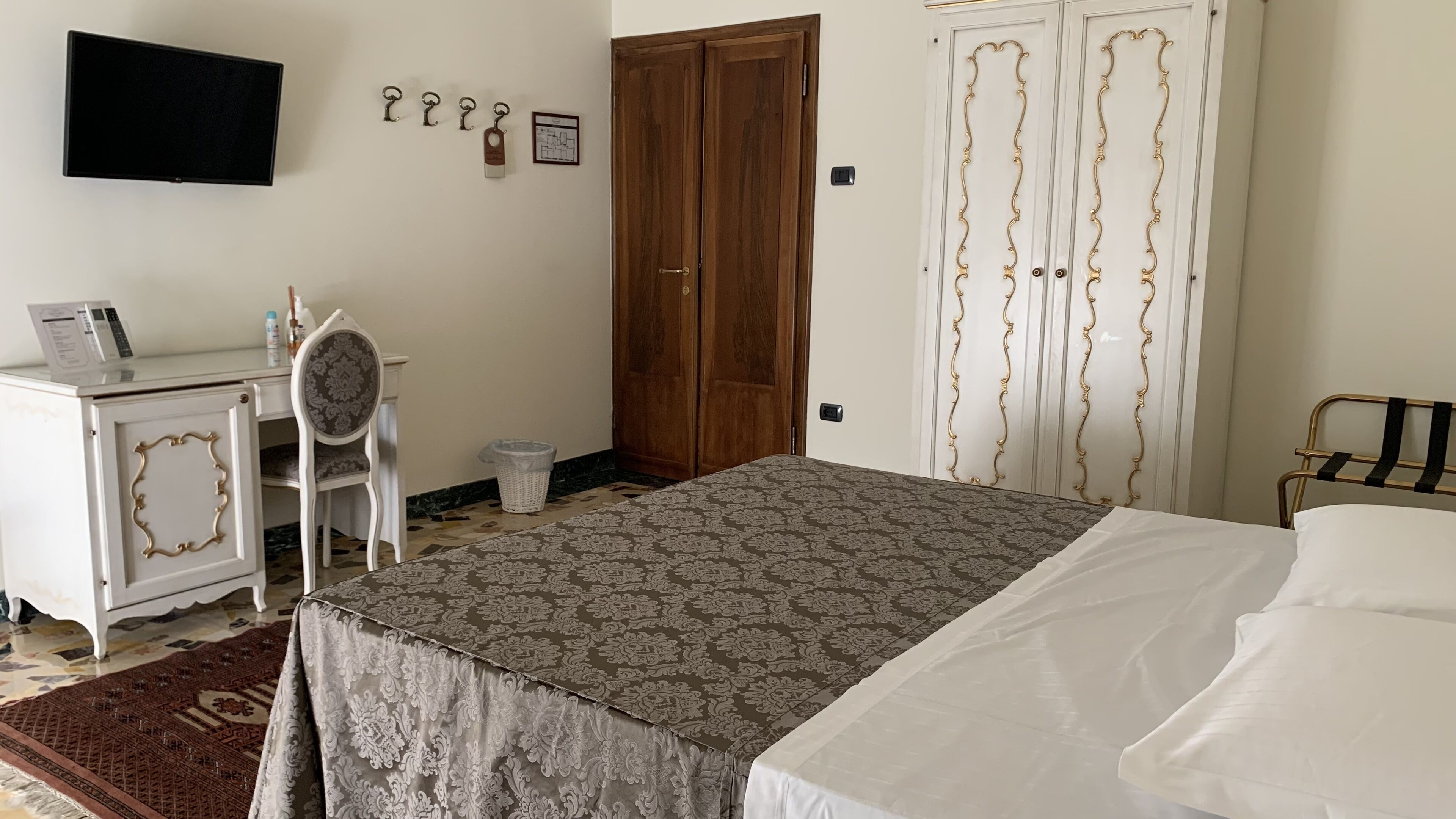 A bedroom with a bed, a desk with a chair, a TV, and a wardrobe.