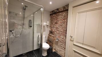 A modern bathroom with a glass-enclosed shower, a toilet, and a brick accent wall.