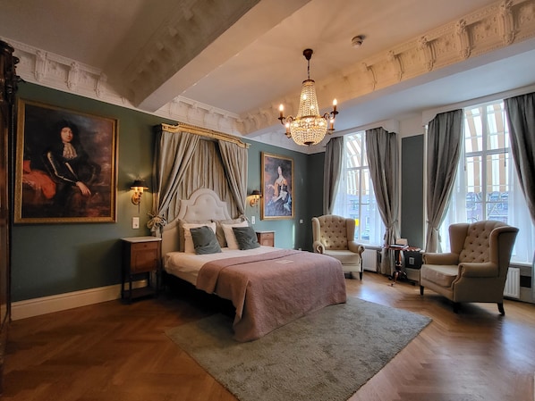 Un dormitorio amplio con una cama grande, dos sillones, una araña y obras de arte en las paredes.