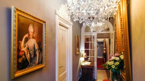 Un couloir orné d’un tableau de style classique, d’un lustre et d’un miroir avec un cadre doré.