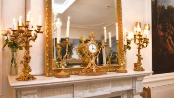 Une vaste pièce agrémentée d’un grand miroir décoratif, d’une cheminée blanche et de plusieurs chandeliers illuminés.