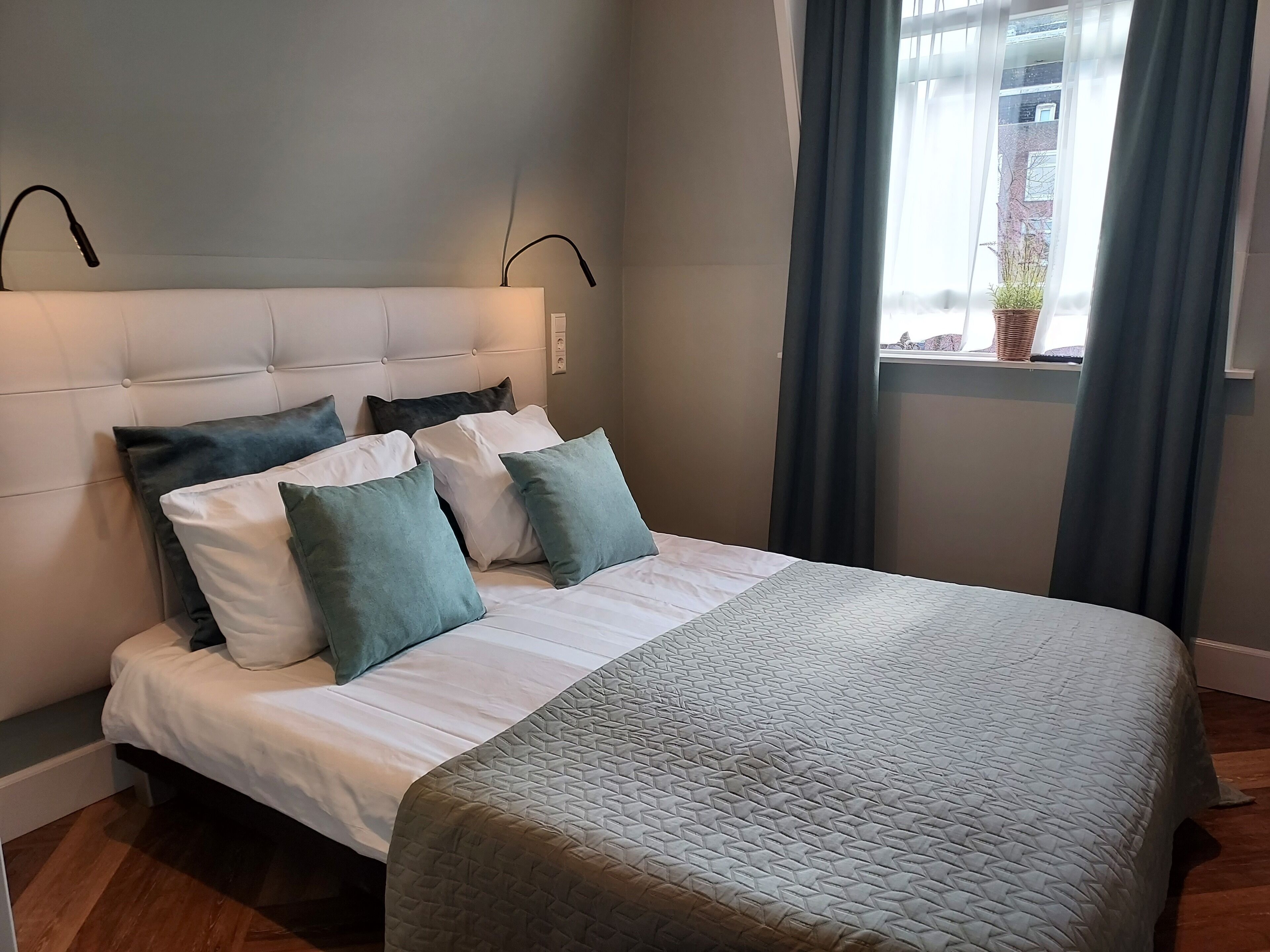 Een opgemaakt bed met een bedspreider met patroon, een gestapeld hoofdbord en meerdere kussens.