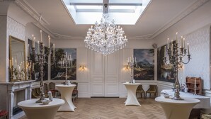 Une vaste pièce dotée d’un plafond haut, d’un grand lustre et de plusieurs tables ornées de bougies.