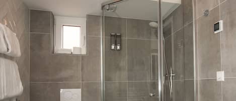 A modern bathroom with a glass-enclosed shower, a toilet, and a vanity with a towel rack.