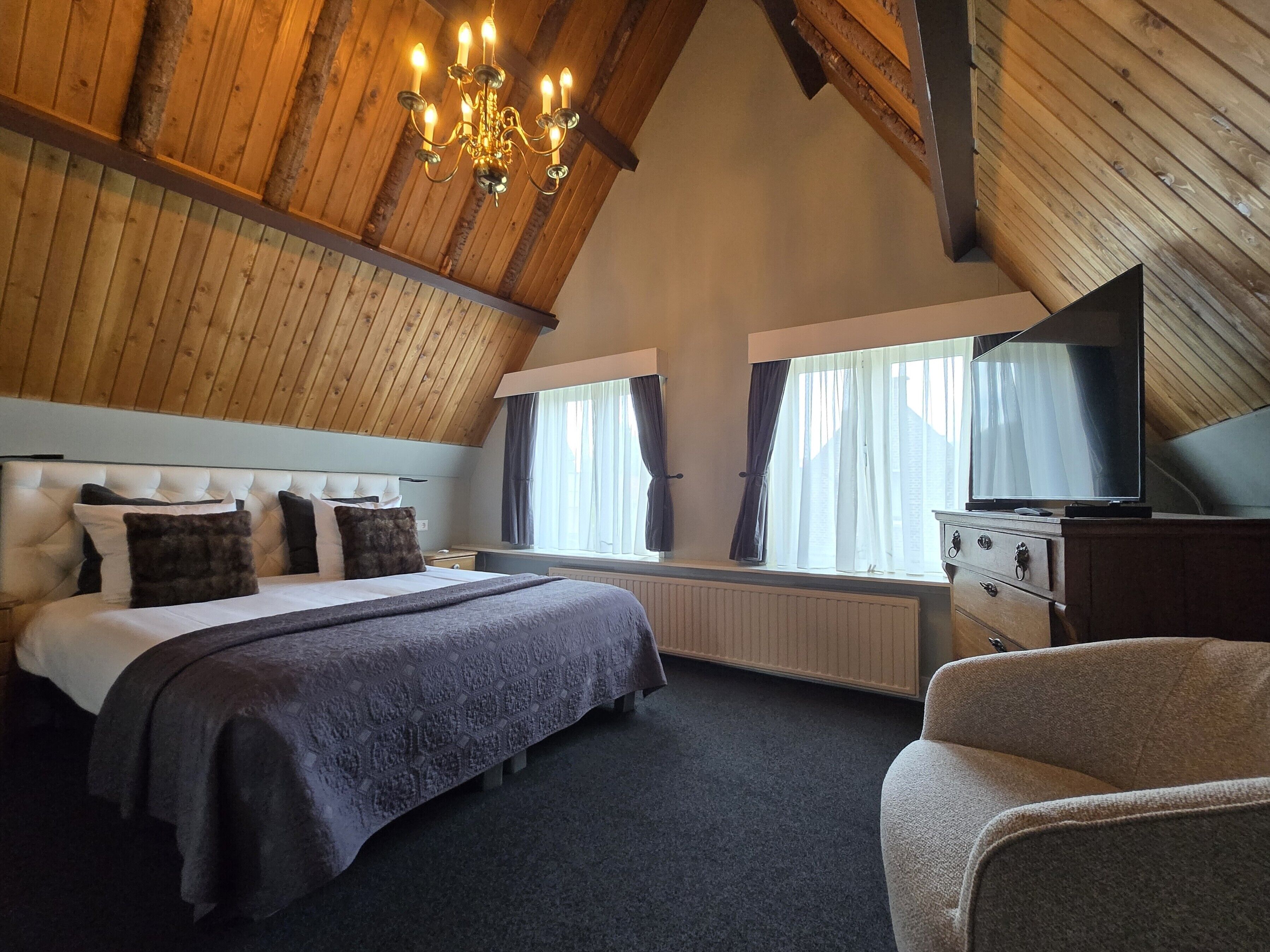 Une chambre à coucher avec un grand lit, une commode, un téléviseur et un lustre.