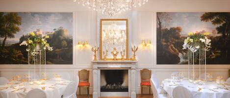 Un comedor formal con manteles blancos, candelabros y cuadros en las paredes.