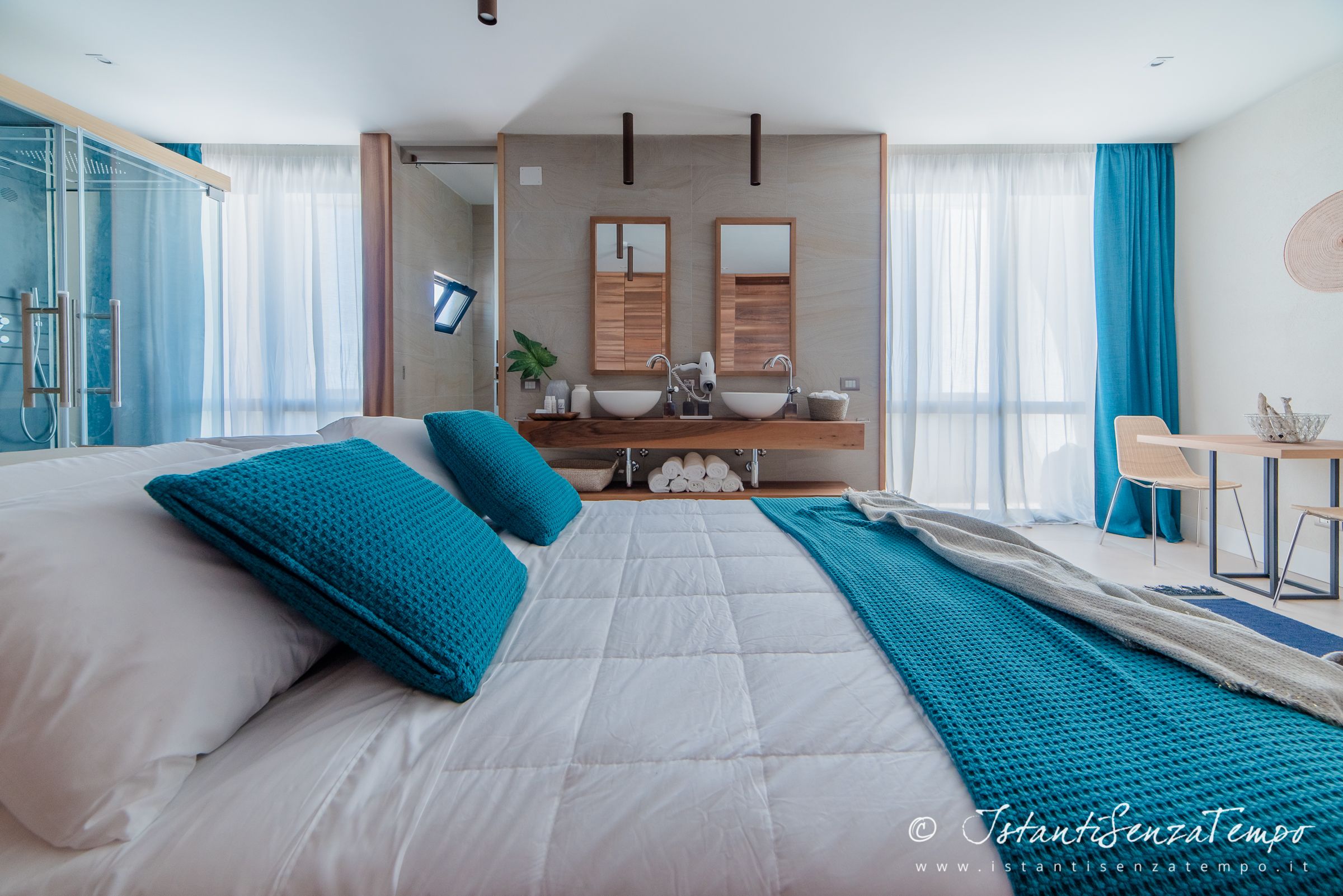 Ein modernes Hotelzimmer mit einem großen Bett, einem Schreibtisch und einem Badezimmer mit Dusche und zwei Waschbecken.