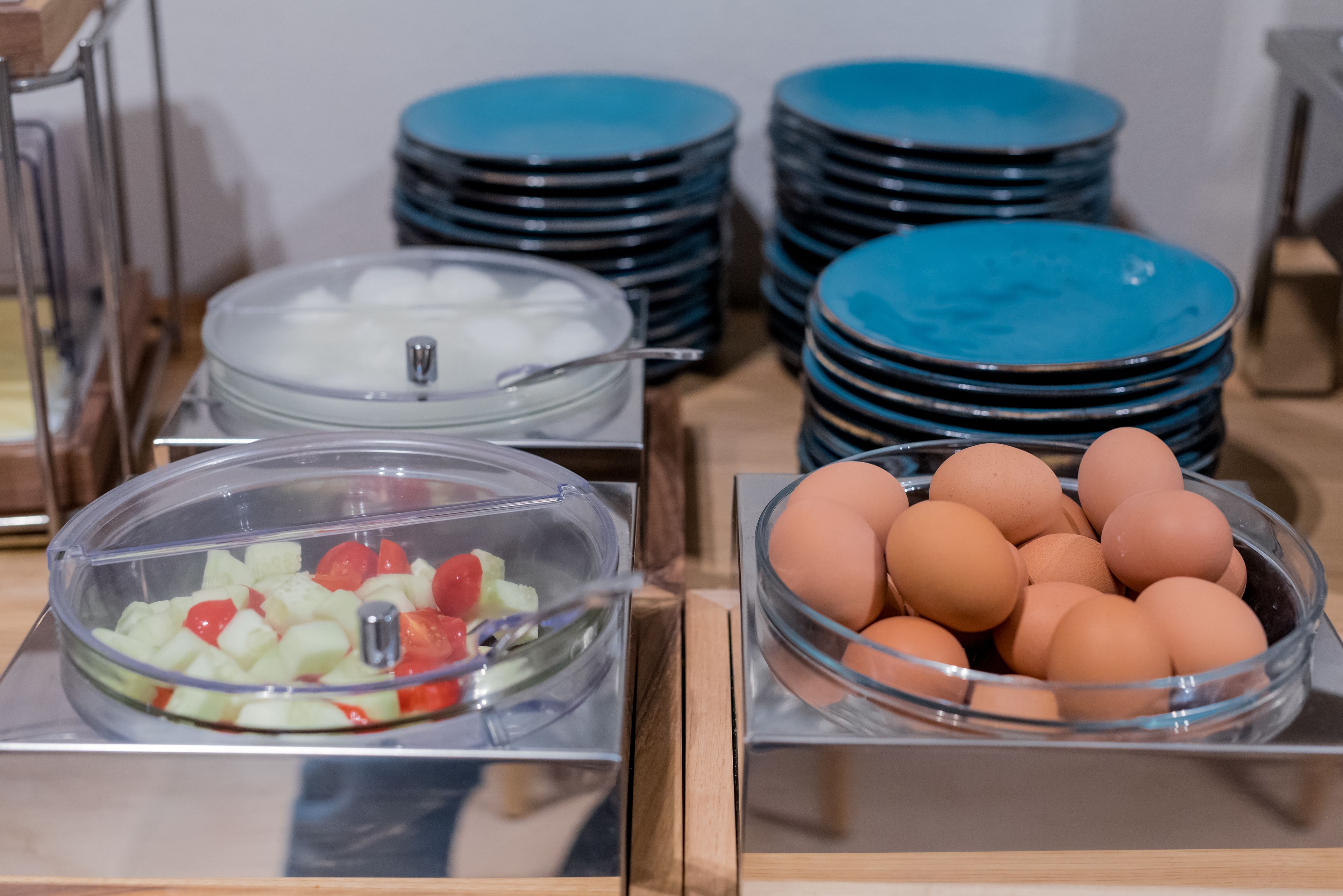 A buffet setup with clear glass bowls containing fruits and eggs, and stacks of blue plates.