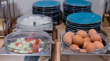 A buffet setup with clear glass bowls containing fruits and eggs, and stacks of blue plates.
