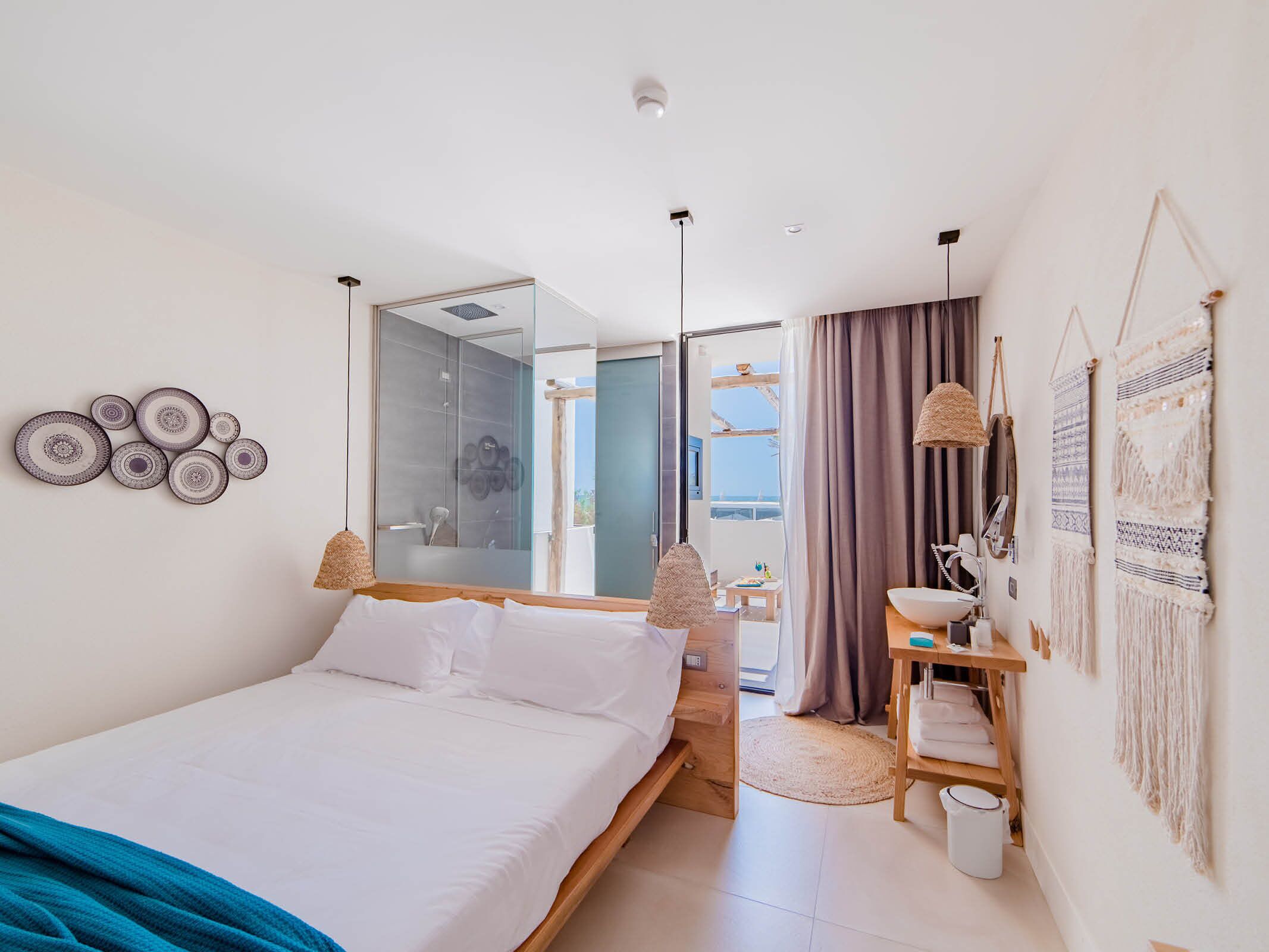 A modern bedroom with a large bed, a mirror, a vanity with a sink, and a view of the outdoors.