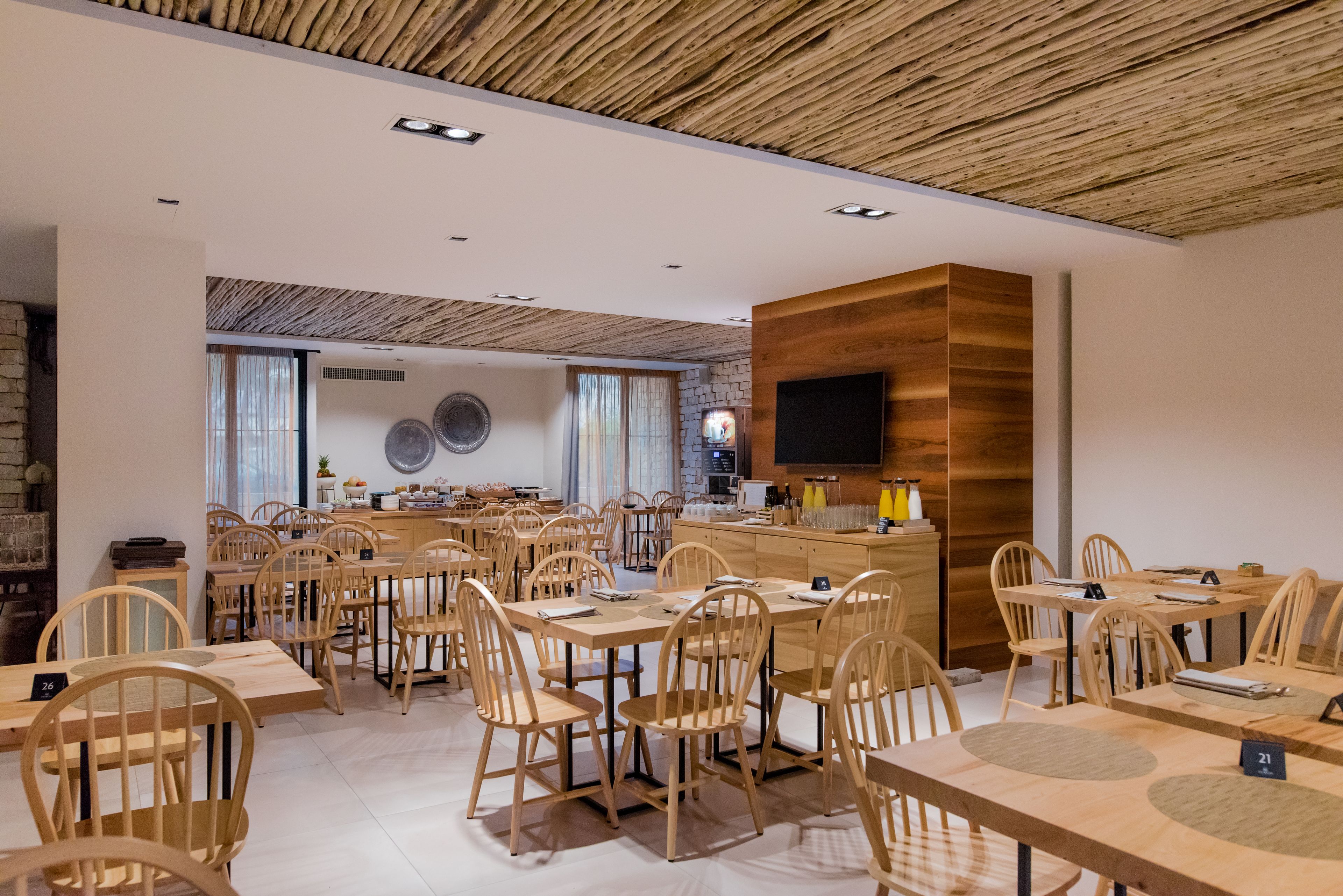 A modern dining area with wooden tables and chairs, a central counter, and a television mounted on the wall.