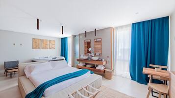 A modern hotel room with a large bed, a sitting area with a chair and table, a bathroom with a vanity and mirror, and a view of the outdoors through large windows.