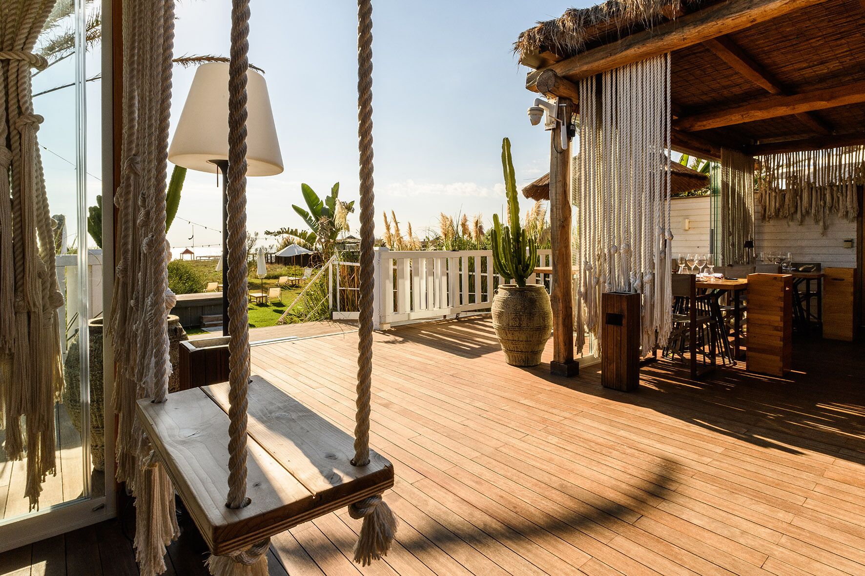 A wooden deck with a swing, a table with chairs, a hanging lamp, and a rustic bar area.