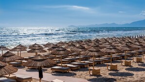 A beach with rows of wooden lounge chairs and thatched umbrellas. - Cumeja - Beach Club & Hotel (Cellole)