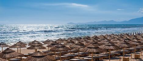 Una playa con filas de sillas de madera y sombrillas de paja.