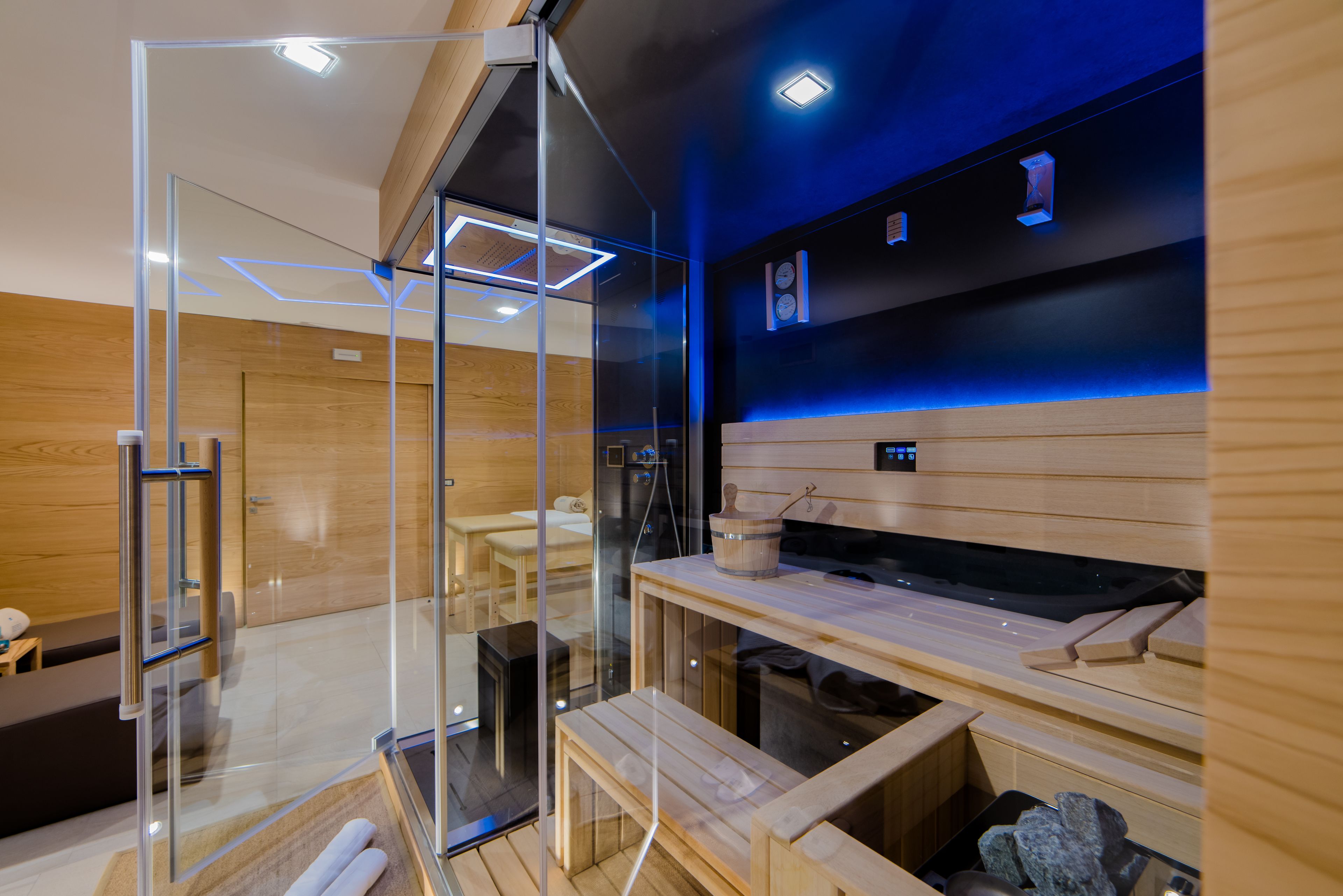 A modern sauna with glass walls, wooden benches, and a blue-lit ceiling.