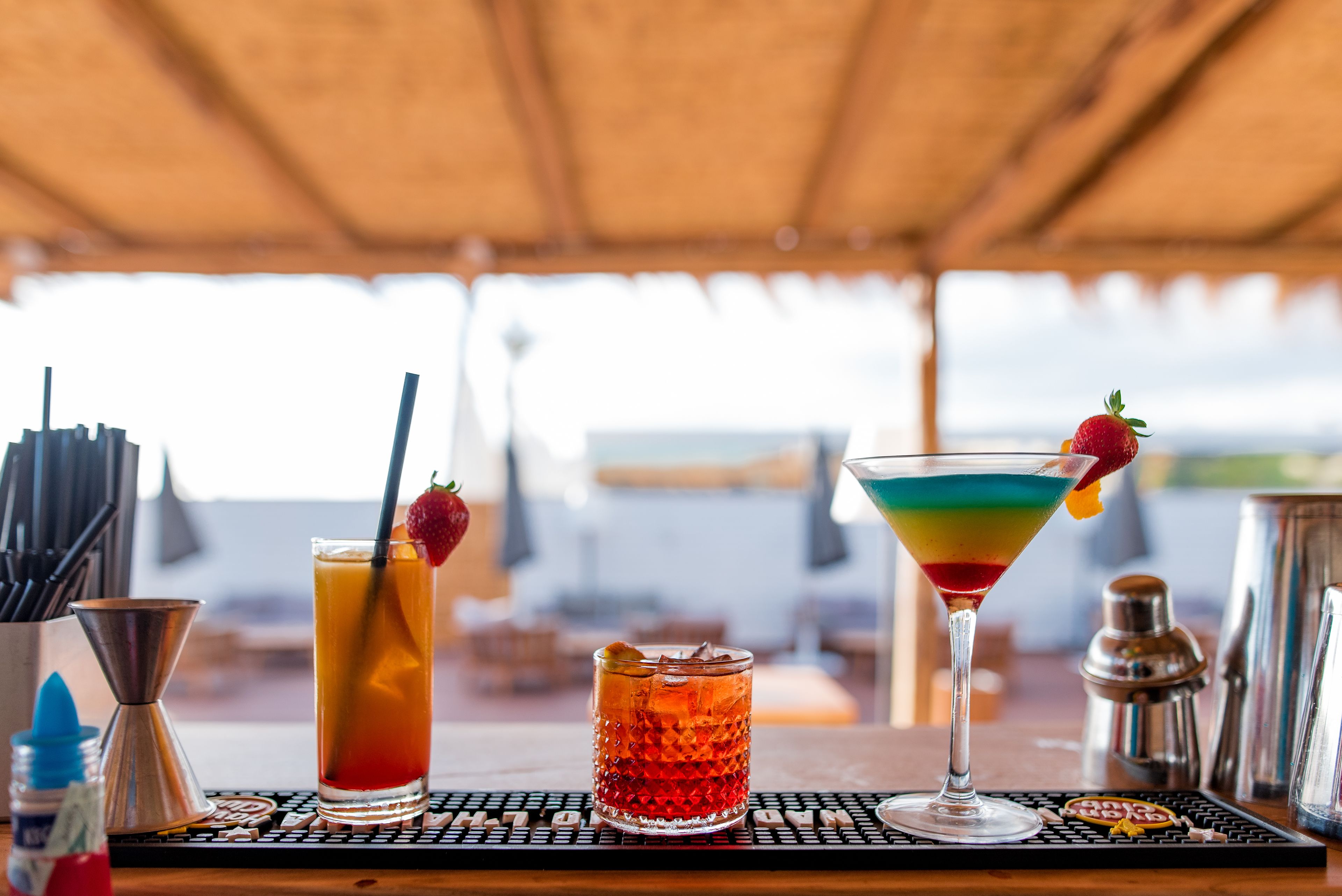 En bardisk med två drinkar, en cocktailshaker och en flaska sås på ett bord.