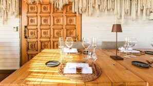 A wooden dining table set with wine glasses, plates, and cutlery, with a woven placemat and a lamp on the table. - Cumeja - Beach Club & Hotel (Cellole)