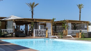 A pool area with wooden deck, lounge chairs, and covered seating areas. - Cumeja - Beach Club & Hotel (Cellole)
