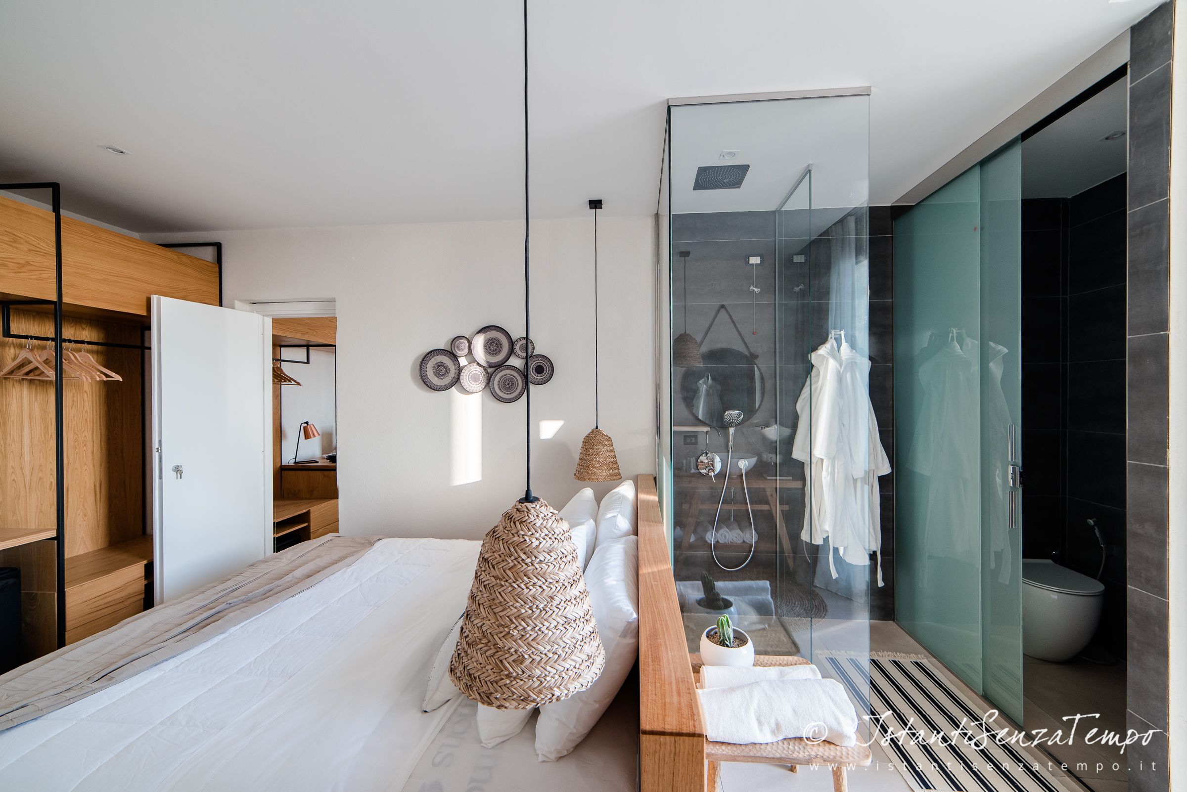 A modern bedroom with a large bed, a wooden wardrobe, a glass shower enclosure, and a hanging light fixture.
