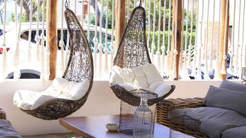 Dos sillones colgantes con cojines blancos, un sofá de mimbre y una pequeña mesa con un florero de cristal.
