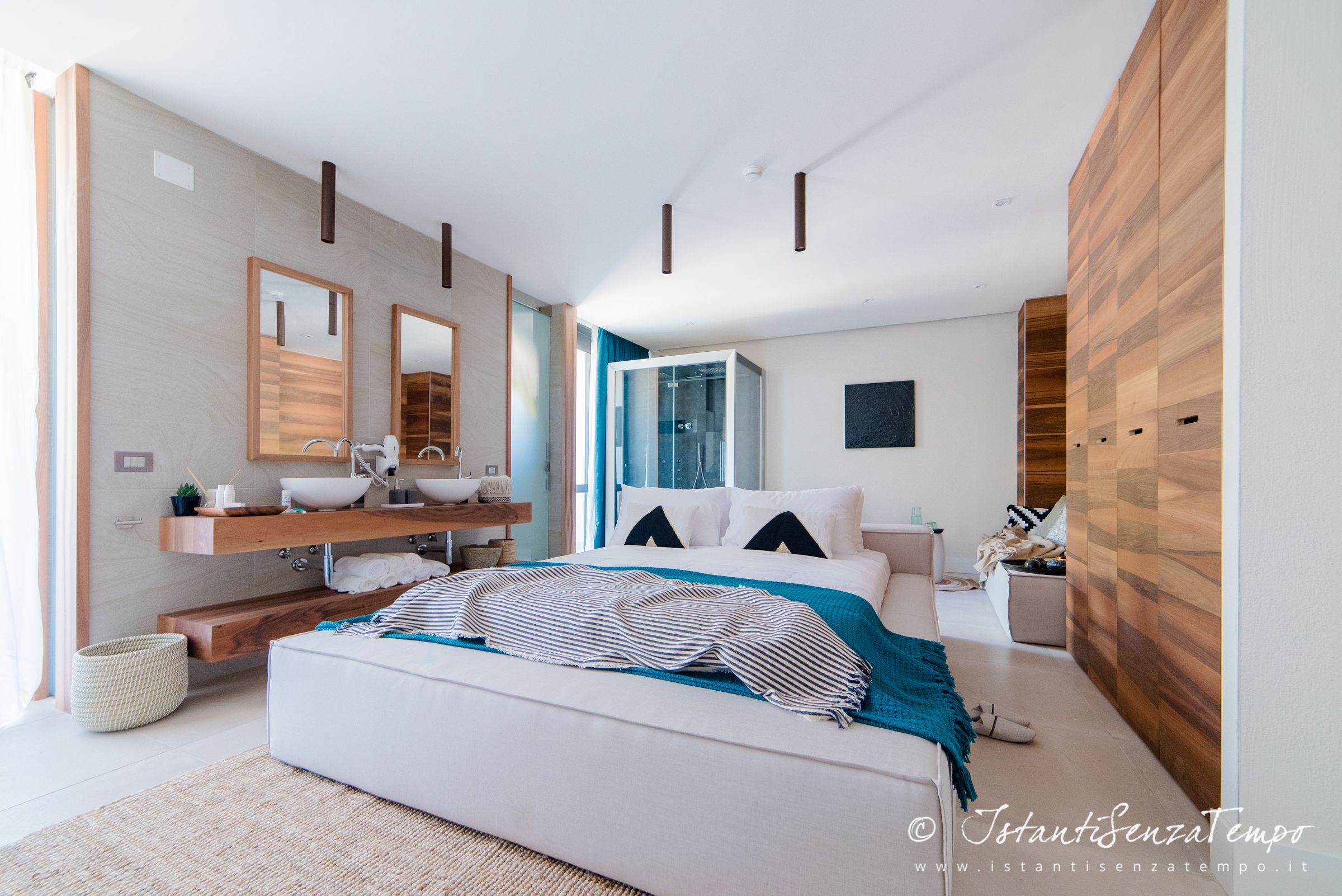 Un dormitorio moderno con una cama grande, un tocador de madera y una zona de ducha integrada.