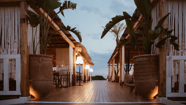 A wooden deck with thatched-roof structures, large potted plants, and a view of the sky. - Cumeja - Beach Club & Hotel (Cellole)