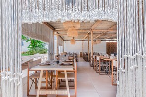 A spacious dining area with long wooden tables and chairs, a ceiling with hanging woven light fixtures, and a view of greenery outside. - Cumeja - Beach Club & Hotel (Cellole)