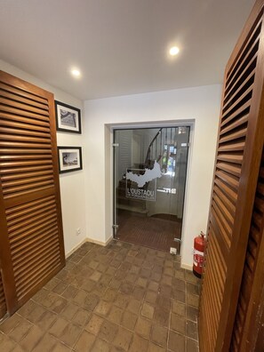 A hallway with a tiled floor, wooden slatted doors, and framed pictures on the wall. - L'oustaou de Porquerolles (Hyères)