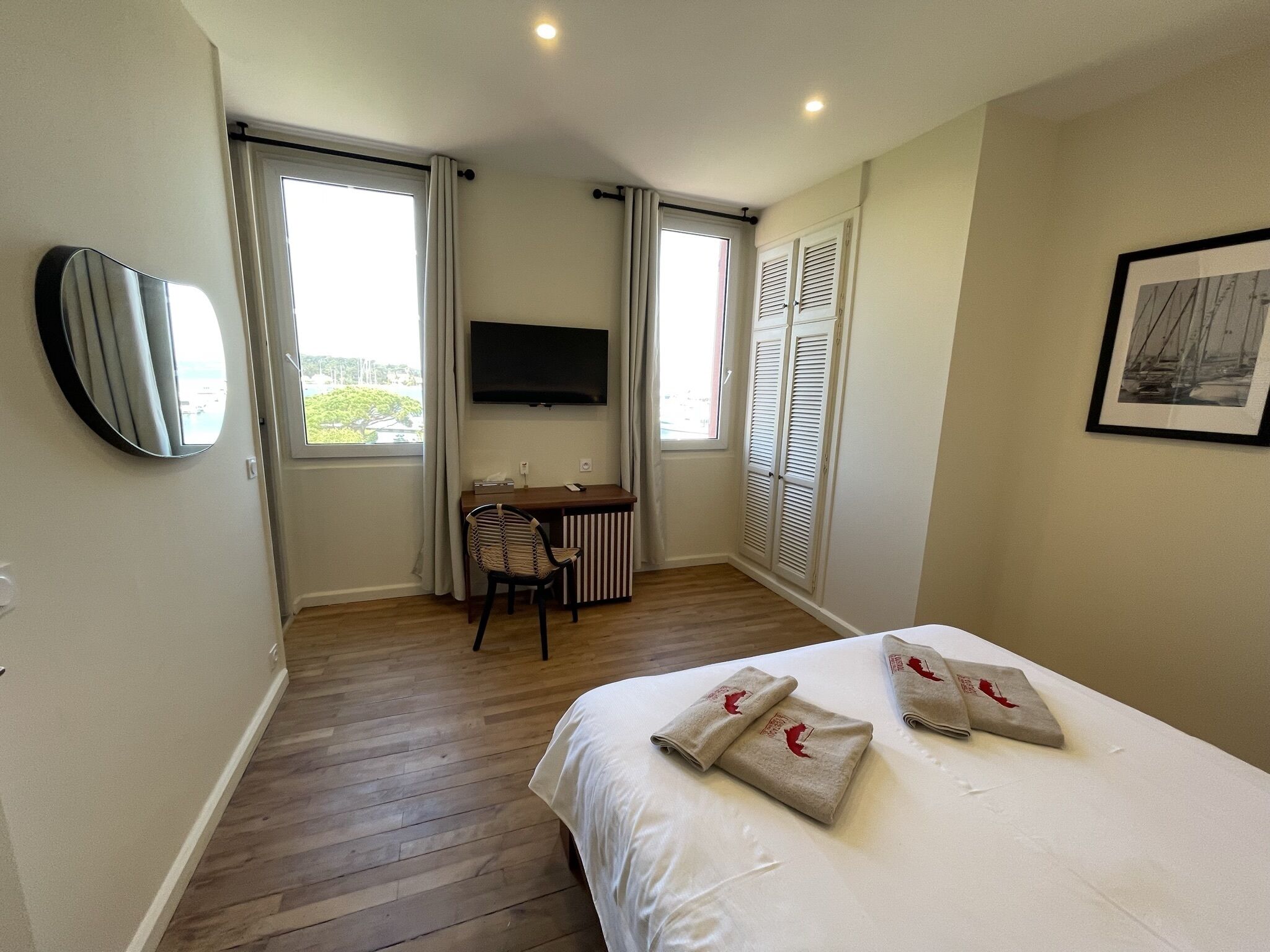 A hotel room with a bed, a desk, a chair, a TV, and a window with shutters.