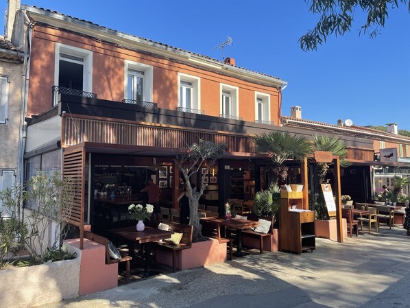 An outdoor seating area with tables and chairs, a bar, and a sign for 'L'OUSTAOU'. - L'oustaou de Porquerolles (Hyères)