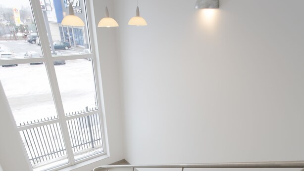 A modern staircase with a metal railing, a white wall, and a window with a view of a parking lot. - Arcus Premium Hostel (Warsaw)