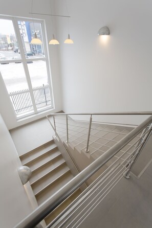 A modern staircase with a metal railing, a white wall, and a window with a view of a parking lot. - Arcus Premium Hostel (Warsaw)