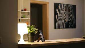 A reception desk with a lamp, a potted plant, a framed picture, and a wall art piece. - Arcus Premium Hostel (Warsaw)