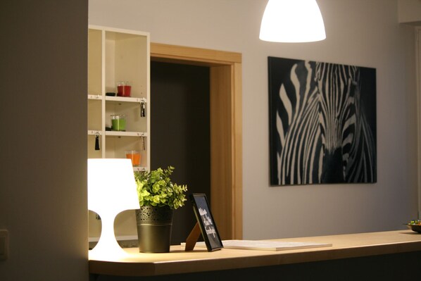 A reception desk with a lamp, a potted plant, a framed picture, and a wall art piece. - Arcus Premium Hostel (Warsaw)