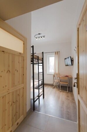 A room with a bunk bed, a desk with a chair, a window with curtains, and a mounted television. - Arcus Premium Hostel (Warsaw)