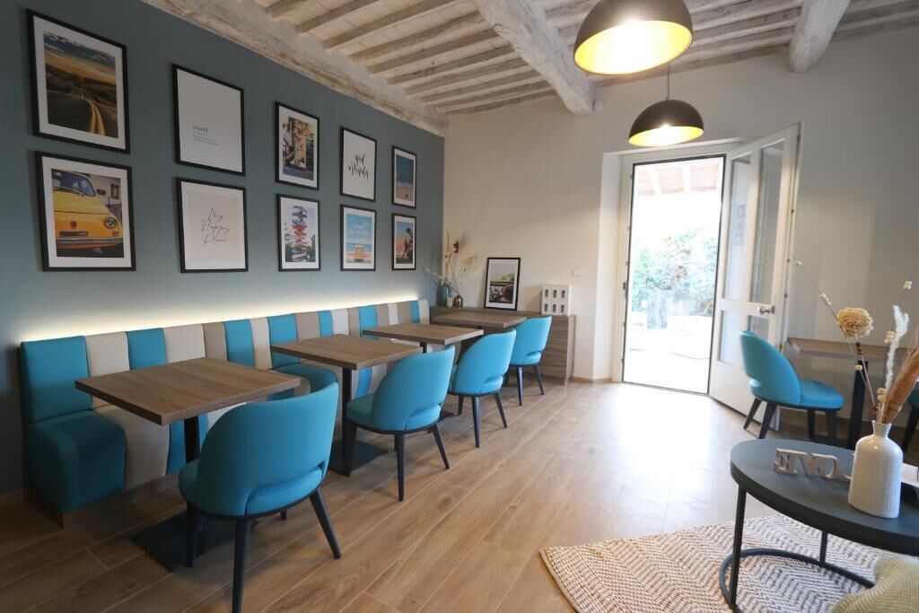 Interior de restaurante con mesas de madera y sillas azules, una pared con cuadros enmarcados y una puerta que da al exterior.
