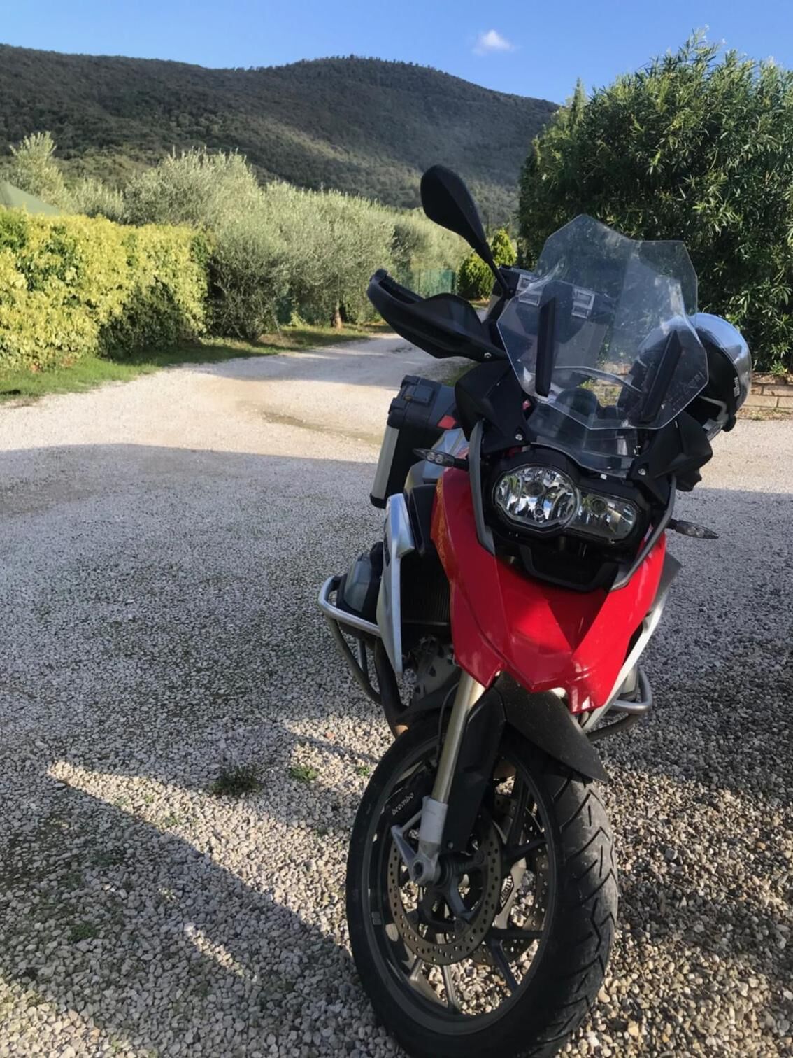 Una motocicleta roja estacionada en un camino de grava con montañas al fondo.